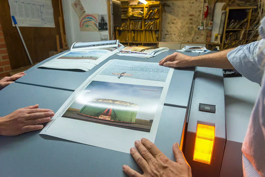 Two people reviewing printed proofs of the Brighton and Hove Calendar at a print press, checking image quality and layout before final production.